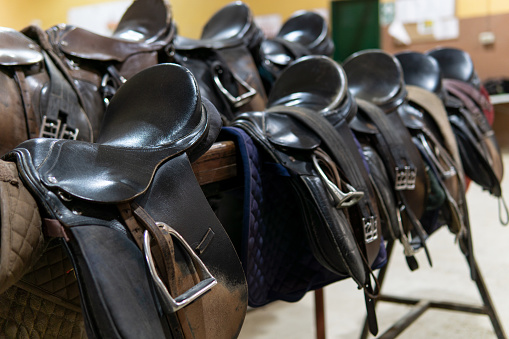 Close up of several horse saddles in a stable, copy space
