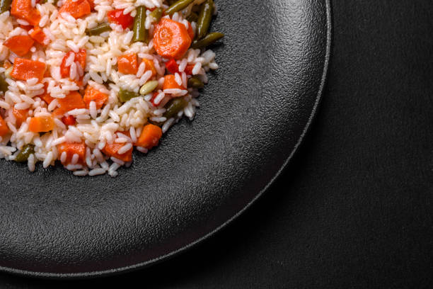 Delicious fresh risotto with vegetables, spices and herbs on a black plate on a dark concrete background