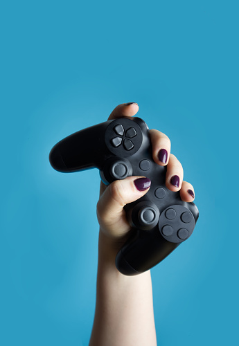 A female hand holds a controller from a video console on a blue background close-up