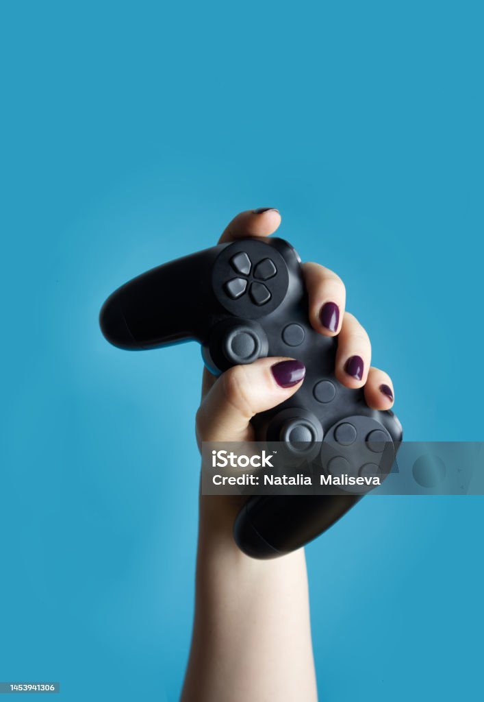 A female hand holds a controller from a video console on a blue background close-up Game Controller Stock Photo
