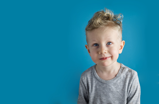 Portrait of a  blue-eyed and fair-haired toddler boy on a blue background close-up