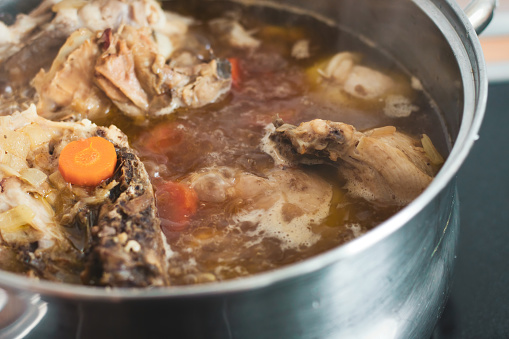 Close-up shot of chicken soup broth bubbling and boiling in a large steel kitchen pot
