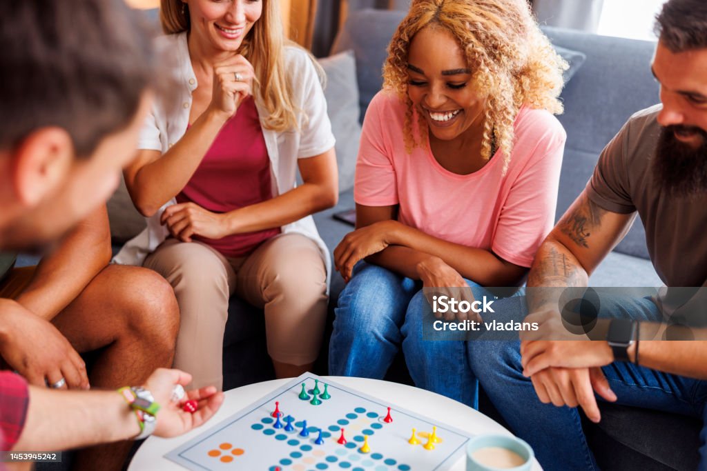 Friends playing ludo Group of cheerful young friends having fun playing ludo board game while spending time together at home Board Game Stock Photo
