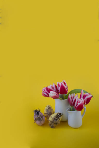 istock Two vases with tulips next to decorated Easter eggs on a yellow background copy space 1453946309