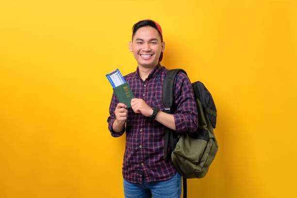 istock Cheerful young Asian man with backpack holding passport and flight tickets isolated over yellow background. Tourism and holiday trip concept 1453946974
