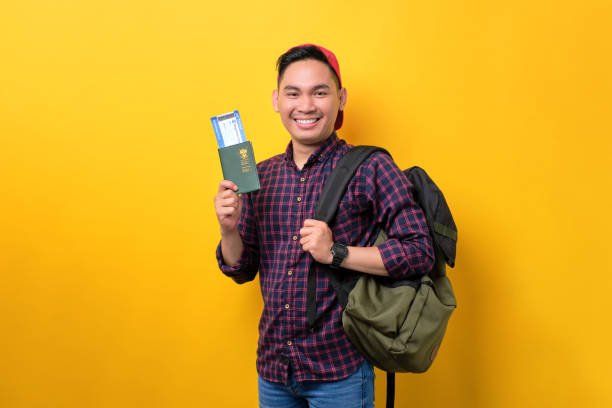 istock Cheerful young Asian man with backpack holding passport and flight tickets isolated over yellow background. Tourism and holiday trip concept 1453946979