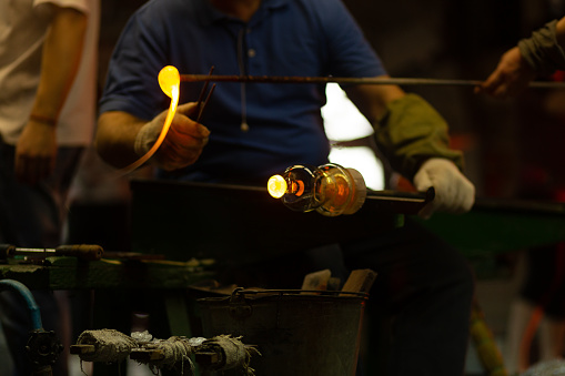 A glass blower is working on the manufacture of glass vases and glasses. Trimming excess glass from the product. Up to 20 workers can be involved simultaneously in the production of particularly complex products.