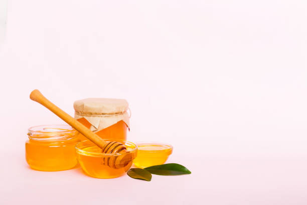 istock Honey in jar with leaves and honey dipper on colored background top view with copy text 1453949817