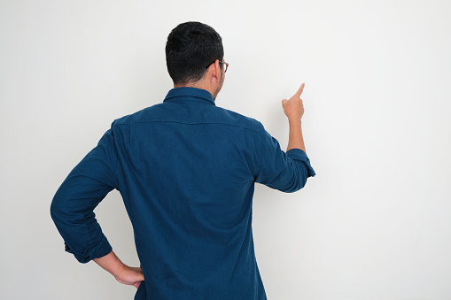 Back view of Adult man pointing to white wall in front of him