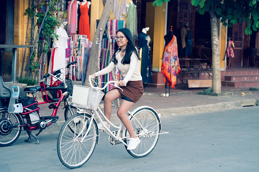 smiling young vietnamese woman riding bicycle  in old town of Hoi An, Vietnam