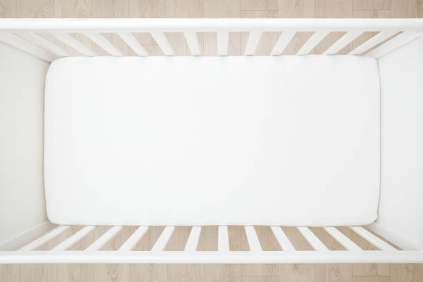 Empty baby crib with white mattress on wooden home floor. Closeup. Top down view. stock photo