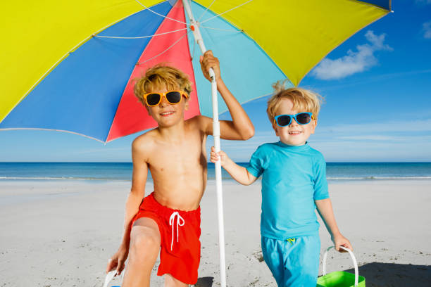 istock Two boys in sunglasses under parasol on a sand ocean beach 1453951662