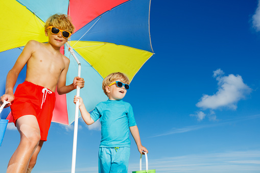 Close portrait of two boys wear sunglasses stand on the sand ocean beach under parasol