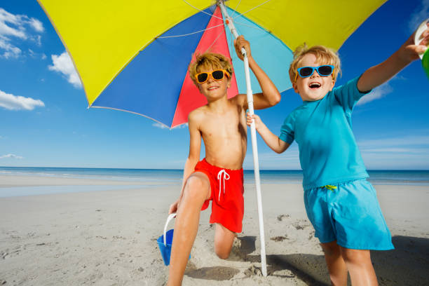 istock Two smiling boys in sunglasses under parasol on an ocean beach 1453951686