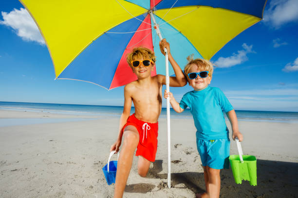 istock Two children in sunglasses under parasol on a sand ocean beach 1453951690