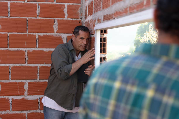 istock Middle aged rural builders install window frame in half-made construction at field in afternoon 1453953596
