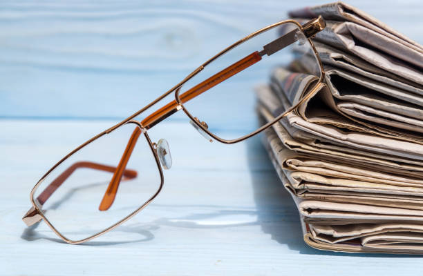 istock Reading glasses and a stack of newspapers on blue wooden shelf 1453958831