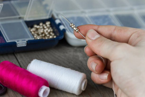 Adult hands using pliers, assembling unique earrings with decorative feather and pencil shaped elements on a clean white table