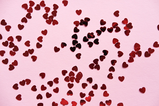 Many small red hearts on a pink background. Holiday concept. Flat lay for your design.