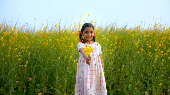 Medium shot of a cheerful Indian kid/child holding mustard/Sarso flowers with a toothy smile - village lifestyle