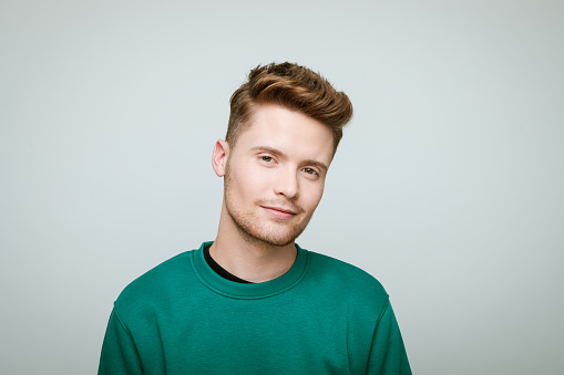 Portrait of young confident male 18-20 years old with crossed arms on grey studio background. Handsome guy in pink t-shot with curly hair looking at camera. Lifestyle, youth concept