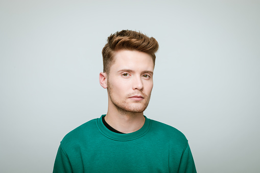 Portrait of young man wearing green blouse looking at camera. Studio shot against grey background.