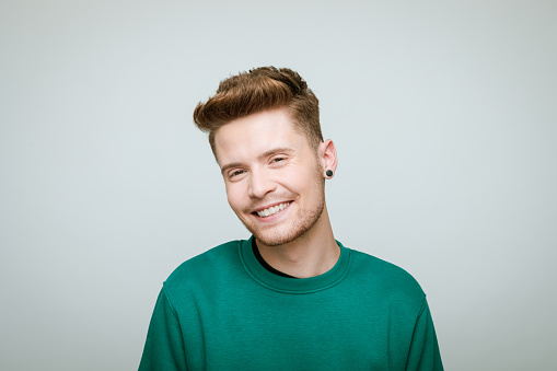 Portrait of young man wearing green blouse smiling at camera. Studio shot against grey background.