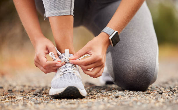 schuhe, fitness und bewegung mit einer sportlerin, die ihre schnürsenkel vor dem training, laufen oder einem training bindet. hände, gesundheit und cardio mit einer läuferin oder athletin, die sich auf einen ausdauerlauf vorbereitet - schuhwerk stock-fotos und bilder