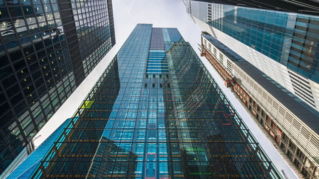 Time lapse Low angle of tall corporate buildings skyscraper with reflection of clouds among high buildings and glass elevator in building center
