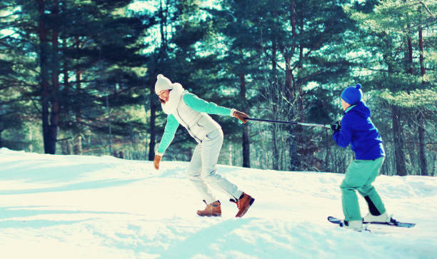 Cheerful mother having fun with skiing child son in winter forest stock photo