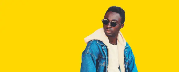 Portrait of stylish young african man model looking away wearing denim jacket isolated on yellow background, blank copy space for advertising text
