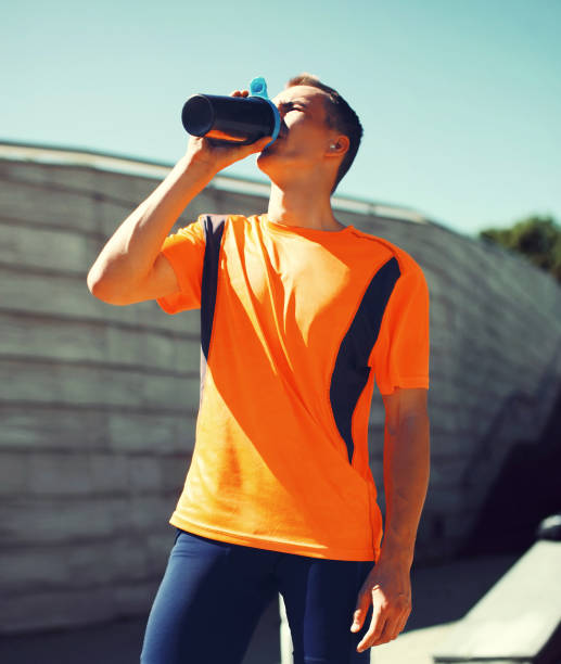 Portrait of tired young runner man drinking from bottle the water or protein shake, male sportsman resting after hard training in the city stock photo