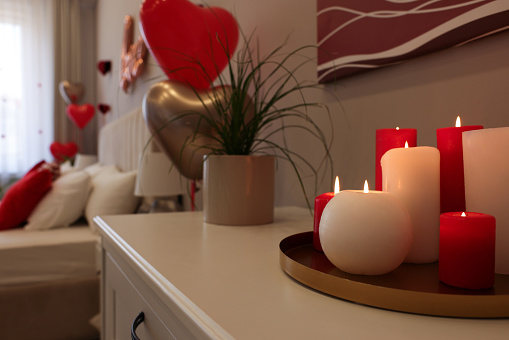Burning candles on white table in room decorated for Valentine's Day