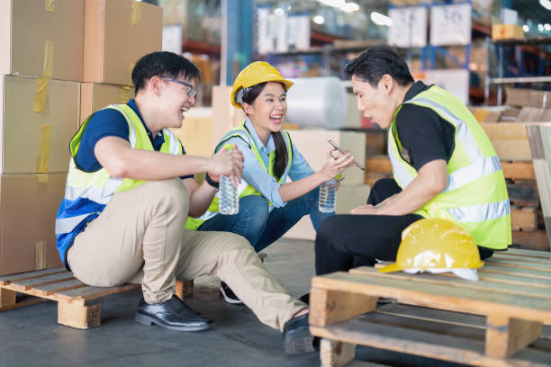 istock Staff in large storage warehouse together sit back relax funny laughing check mobile phone 1453970533