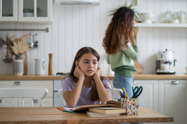 istock Sad frustrated schoolgirl sitting at kitchen table with textbooks, needs help with homework 1453970625