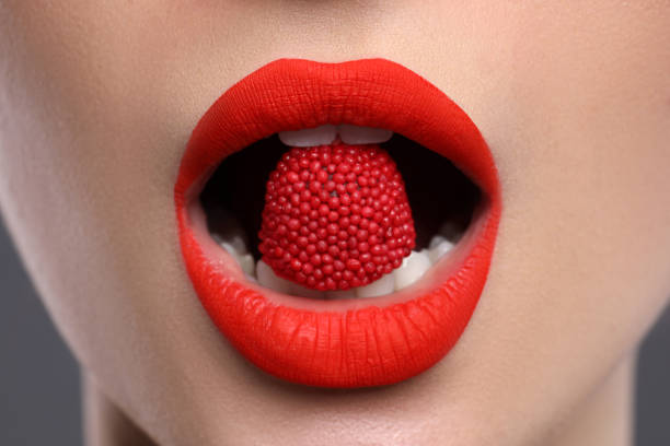 istock Beautiful young woman with red lips makeup eating candy, closeup 1453971225