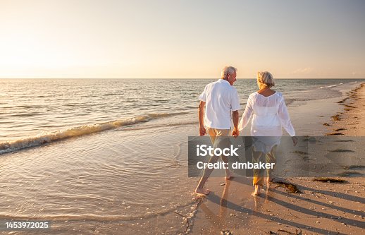 istock Happy Senior Old Retired Couple Walking Holding Hands on Beach at Sunset 1453972025