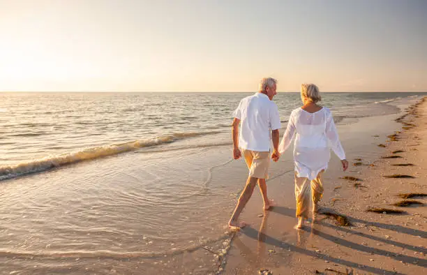 Photo of Happy Senior Old Retired Couple Walking Holding Hands on Beach at Sunset