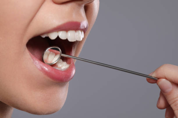 istock Dentist examining woman's teeth with mirror on grey background, closeup 1453972602