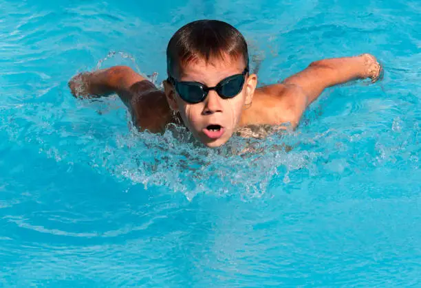 Photo of Boy swimmer swimming butterfly stroke in pool in action. Young athlete swim in swimming pool, training before competition. Water sports, learn to swim school classes for children
