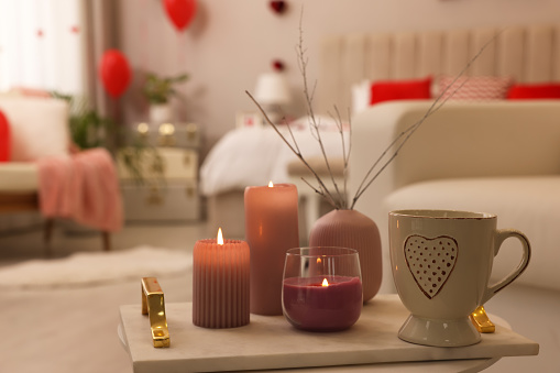Burning candles and cup of hot drink on table in room