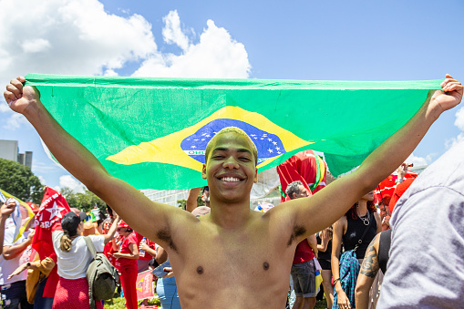 Brasília, DF, Brazil – January 01, 2023: A boy protecting himself from the strong sun using a Brazilian flag. Photo taken during President Lula's inauguration event.