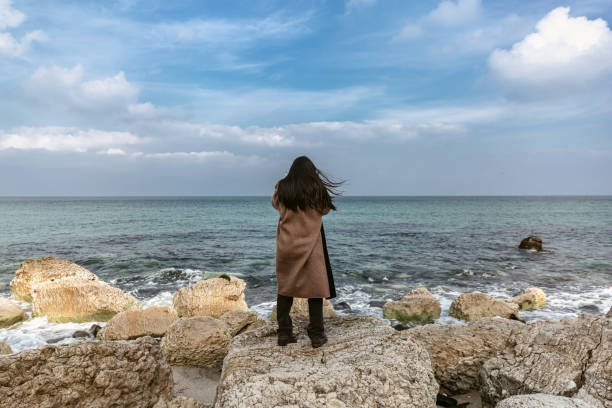istock Woman standing on a cliff overlooking an ocean and spectacular view 1453980130