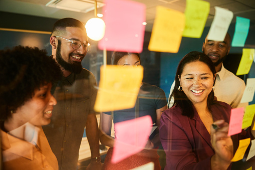 Group of diverse businesspeople smiling during a brainstorming session using adhesive notes on a glass wall in an office