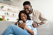 African american couple sitting on couch, using cellphone