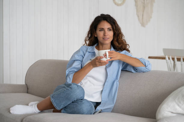istock Casual carefree woman with mug sits on couch having fun spending time alone thinking about future 1453987754