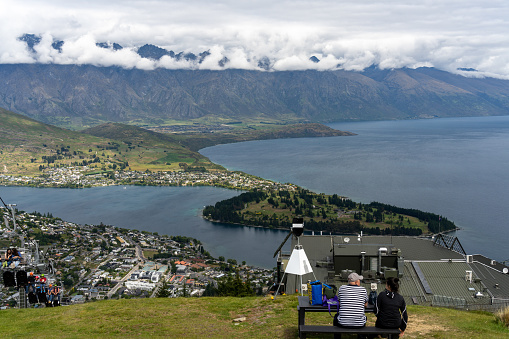 Queenstown, New Zealand - December, 2022: Lake Whakatipu, as viewed from a top of hill. a couple is watching the panoramic view.