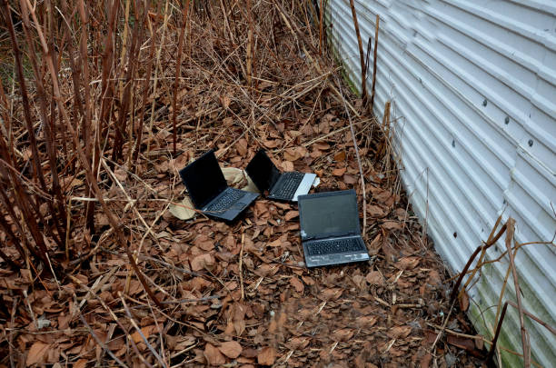 behind a metal fence in the bushes is a secret homeless hacking lair. three laptops are lying on the ground ready to connect. recycling old electrical waste dumped outside the city, personal data, stolen detrás de una valla de metal en los arbustos hay una guarida secreta de piratería sin hogar. tres computadoras portátiles están tiradas en el suelo listas para conectarse. reciclaje de residuos eléctricos viejos vertidos fuera de la ciudad, datos pers