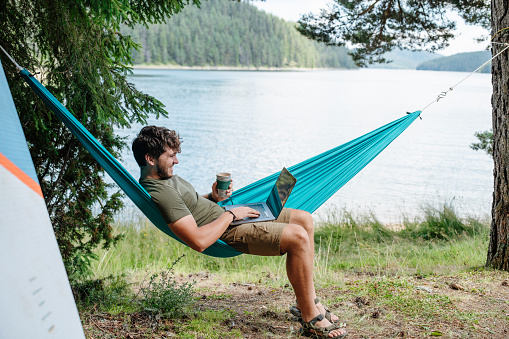 Man balancing between work and camping vacation.Using technology in nature.