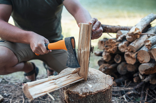 Young man using axe to chop some wood for the campfire.